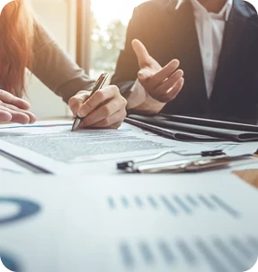 Two people sit at a desk reviewing and signing documents; one is writing while the other gestures, suggesting a discussion or agreement in a business or legal setting at Casillas Insurance in Katy TX.